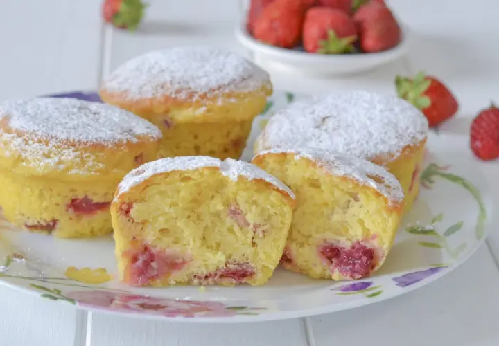 Morbidi muffin alle fragole, cosparsi di zucchero a velo, invitano a un dolce assaggio. Pezzi di fragola succosa si intravedono nell'impasto soffice.