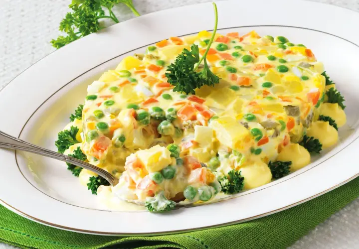 Insalata russa ricetta della nonna: un piatto cremoso con patate, carote, piselli e uova, guarnito con prezzemolo fresco.