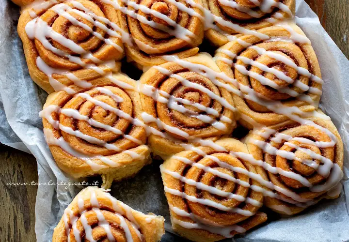 A close-up shot of freshly baked cinnamon rolls drizzled with white icing.