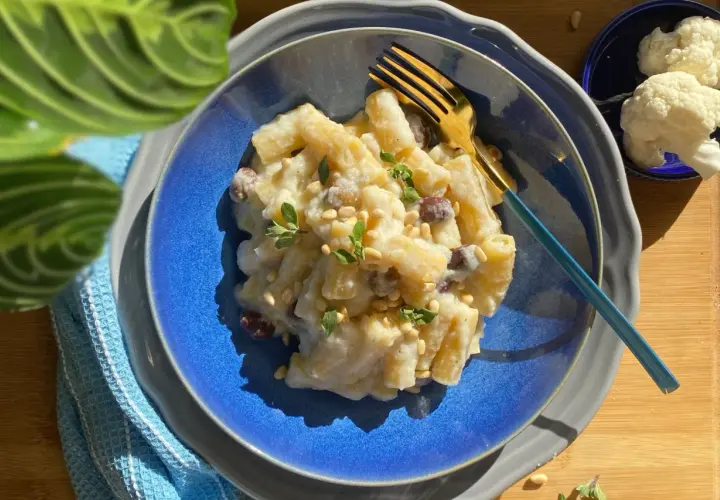 Piatto di pasta e cavolfiore cremoso, guarnito con pinoli e erbe aromatiche, pronto per essere gustato.