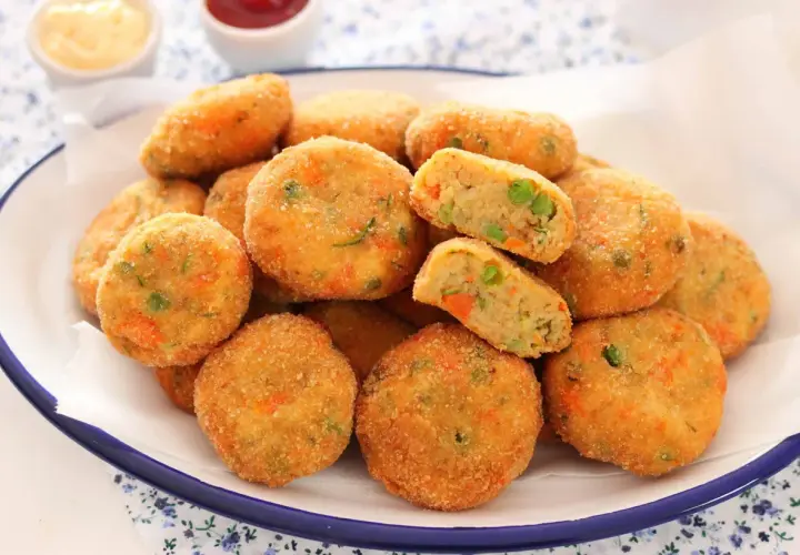 Un piatto pieno di polpette di verdure al forno, dorate e croccanti, con piselli e carote visibili all'interno.