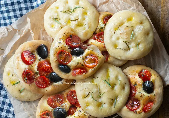 Focaccine in padella, alcune condite con pomodorini e olive, altre con rosmarino e olio. Perfette per uno spuntino.