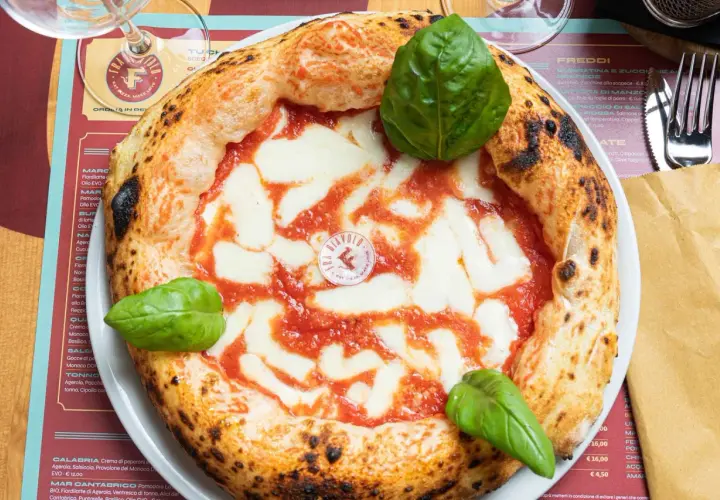 Impasto pizza napoletana con pomodoro, mozzarella filante e basilico fresco. La crosta è alta e alveolata, segno di una lievitazione perfetta.