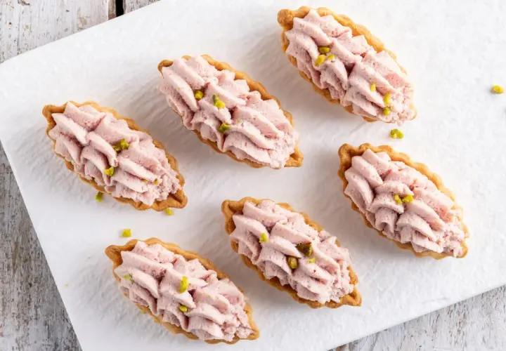 Piccoli cestini di pasta brisée ricetta, ripieni di crema rosa e guarniti con pistacchi.