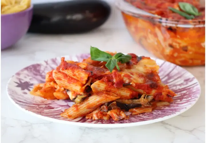 Piatto di pasta alla siciliana con melanzane, pomodoro e basilico, appena sfornata.
