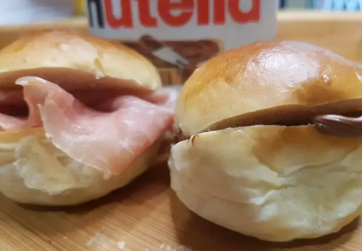 Due panini al latte, uno con prosciutto e l'altro con Nutella, pronti per essere gustati.