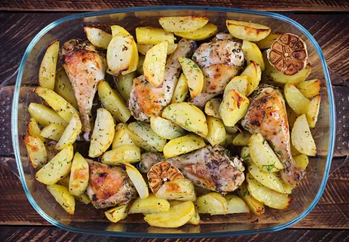 Un succulento pollo e patate al forno, dorati e profumati, in una teglia di vetro.