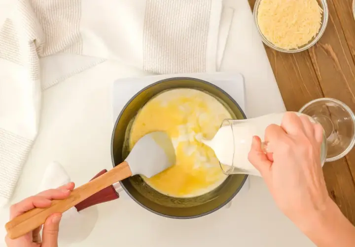 Mani versano latte in una padella con uova e formaggio grattugiato, preparando una deliziosa crema di parmigiano.