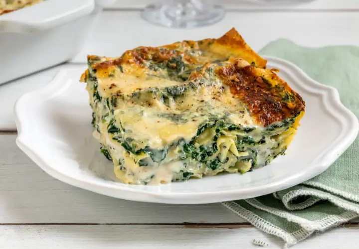 Una fetta di lasagne ricotta e spinaci, dorata al forno, su un piatto bianco.