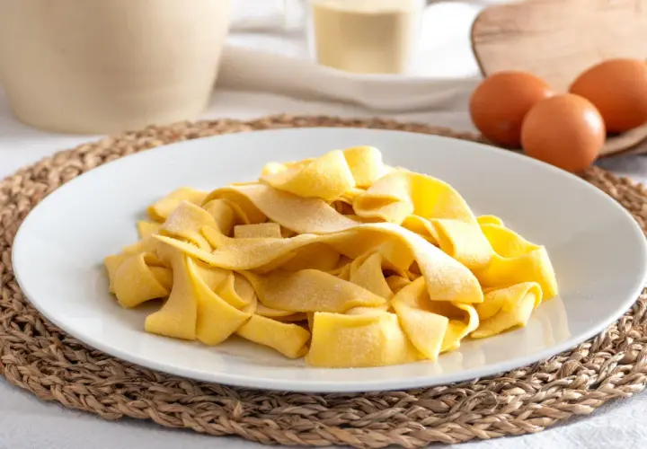 Piatto di pasta fresca fatta in casa, con uova e farina sullo sfondo.