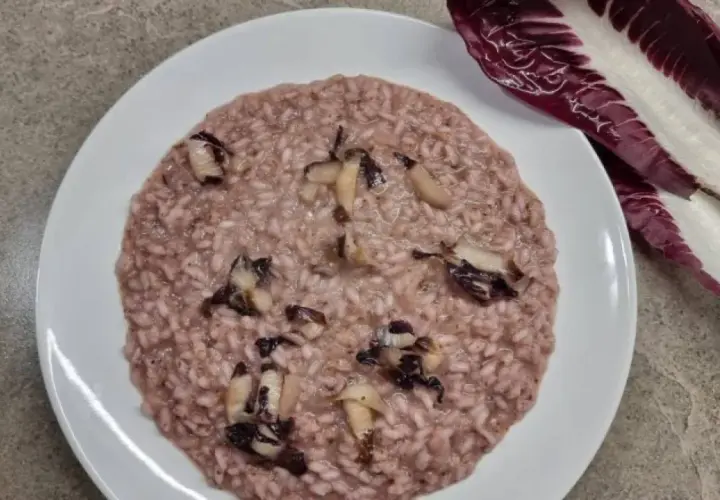 Un cremoso risotto al radicchio rosso, con pezzetti di verdura che spuntano. Accanto, una foglia di radicchio fresco.