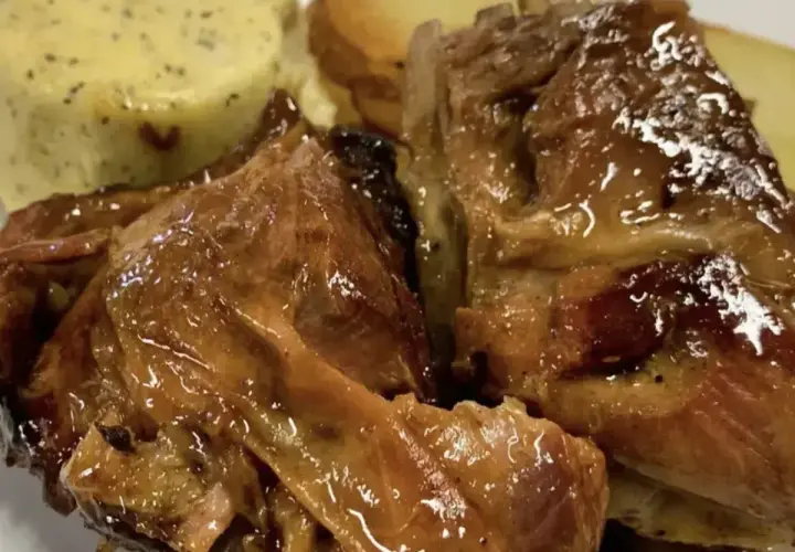 Succulento agnello al forno, dorato e lucido, servito con patate arrosto e una crema verde.