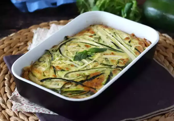 Deliziosa frittata di zucchine al forno, dorata e profumata, guarnita con basilico fresco.
