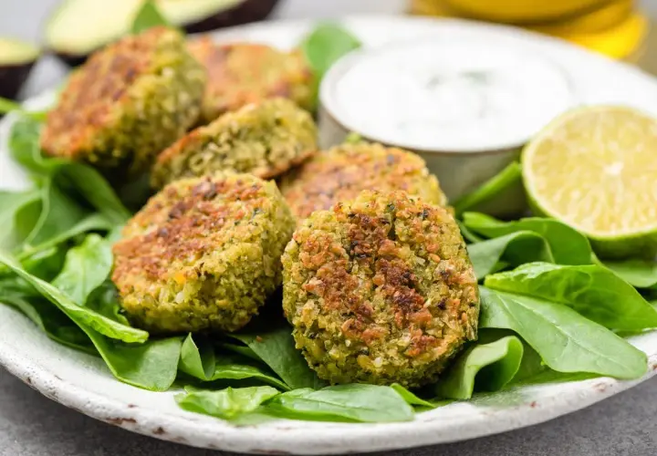 Polpette di spinaci dorate su un letto di spinaci freschi, con una ciotola di salsa e spicchi di lime.