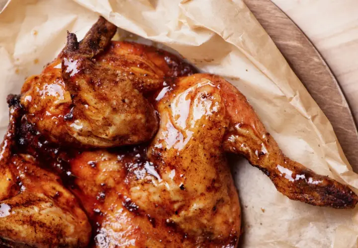 Pollo alla diavola succulento e dorato, con pelle croccante e lucida, servito su carta da forno.