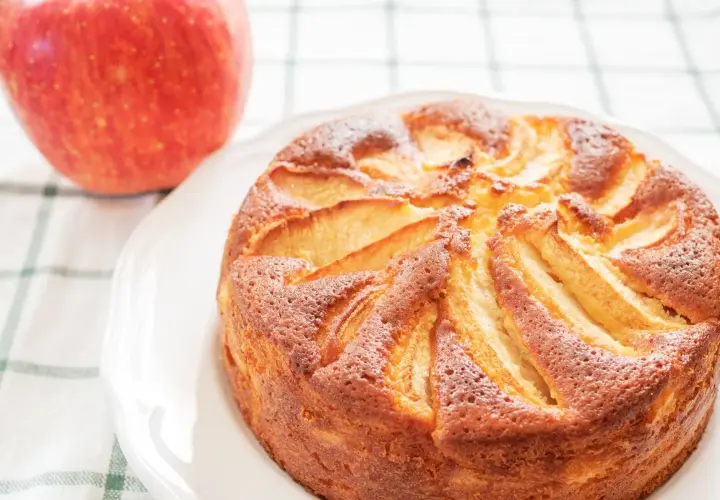 Torta di mele con yogurt, dorata e soffice, con mele a vista. Accanto, una mela rossa fresca.