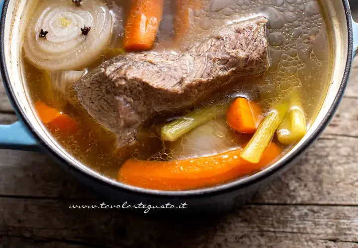 Un pezzo di carne succulenta cuoce lentamente in un brodo di carne aromatico, con carote, sedano e cipolla.