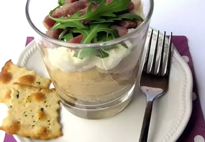 Deliziosa crema di ceci in bicchiere, stratificata con formaggio spalmabile e guarnita con rucola e prosciutto. Servita con cracker croccanti.