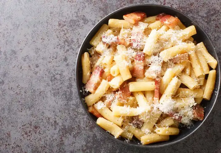 Rigatoni alla gricia fumanti, conditi con guanciale croccante e pecorino romano grattugiato, un classico della cucina romana.