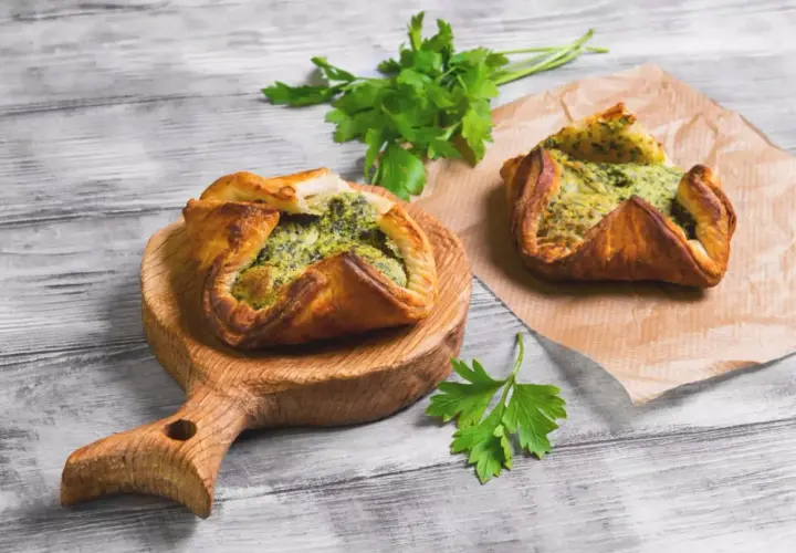 Due fagottini di pasta sfoglia con ripieno verde, uno su tagliere di legno, l'altro su carta forno. Idee su pasta sfoglia cosa mettere dentro.
