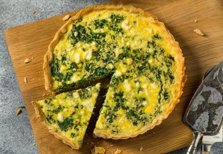 Torta salata ricotta e spinaci dorata e invitante, con una fetta tagliata su un tagliere di legno.