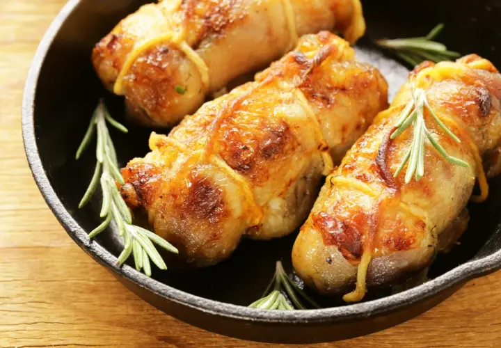 Involtini di pollo dorati e succulenti, legati con spago da cucina e guarniti con rametti di rosmarino, serviti in una padella di ghisa.