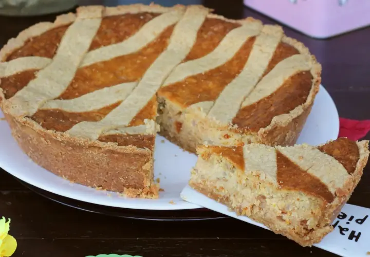 Una pastiera giallo zafferano, con una fetta servita su un piattino, pronta per essere gustata.
