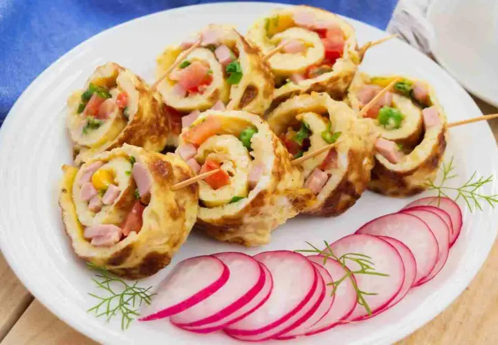 Rotolo di frittata ripieno di prosciutto, pomodoro e verdure, servito con fettine di ravanello.