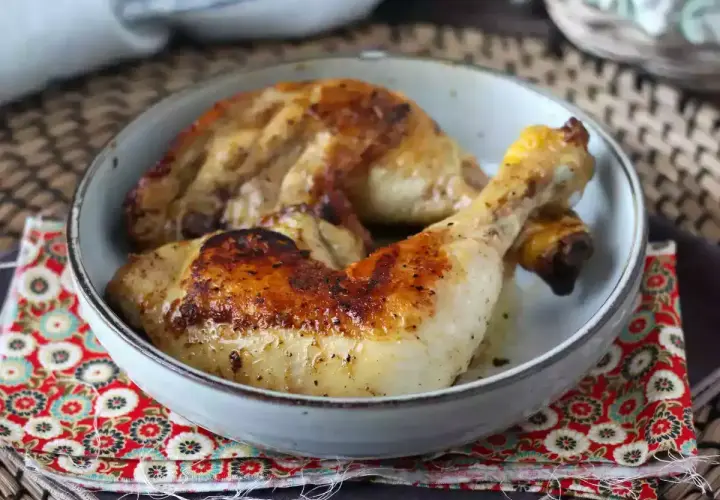 Cosce di pollo in padella, dorate e succulente, servite in una ciotola su un tovagliolo decorato.