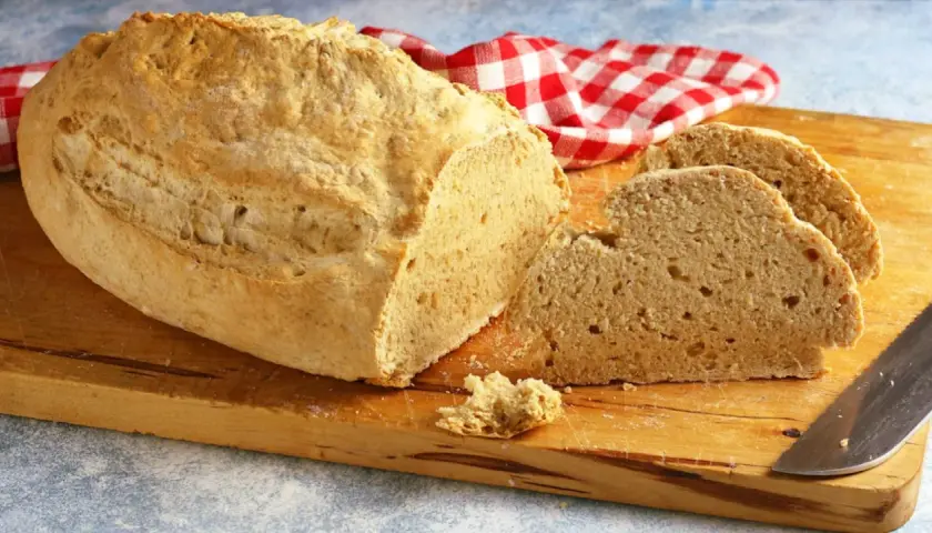 Pane casereccio con lievito istantaneo, tagliato su un tagliere di legno, con un tovagliolo a quadri rossi e bianchi.