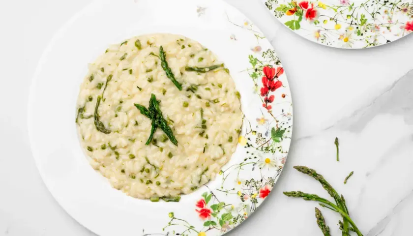 Un cremoso risotto con asparagi selvatici, guarnito con punte di asparago fresco su un piatto fiorito.