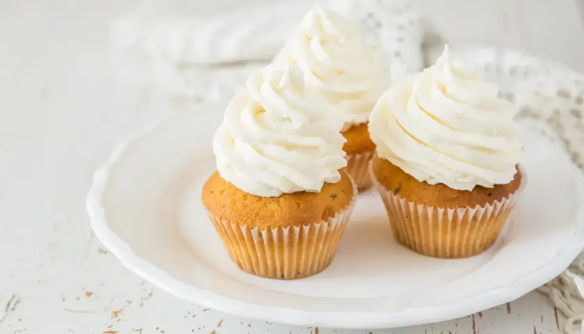 Tre cupcake su un piatto bianco, con abbondante crema al burro soffice e ariosa.