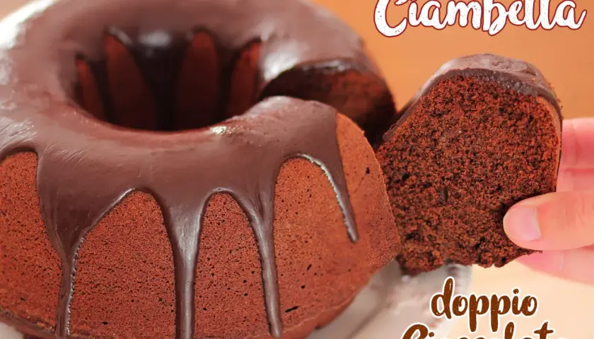 Ciambella al cioccolato, soffice e golosa, con una glassa lucida che cola. Una fetta viene sollevata, mostrando la sua consistenza.