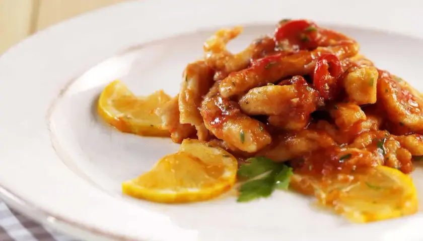 Straccetti di pollo al limone succulenti, conditi con salsa rossa e guarniti con fette di limone e prezzemolo fresco.