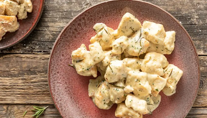 Bocconcini di pollo al latte cremoso, conditi con erbe aromatiche, serviti su un piatto rustico.