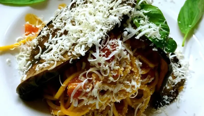 Pasta alla Norma ricetta: spaghetti con melanzane fritte, pomodoro e ricotta salata grattugiata, guarnita con basilico fresco.