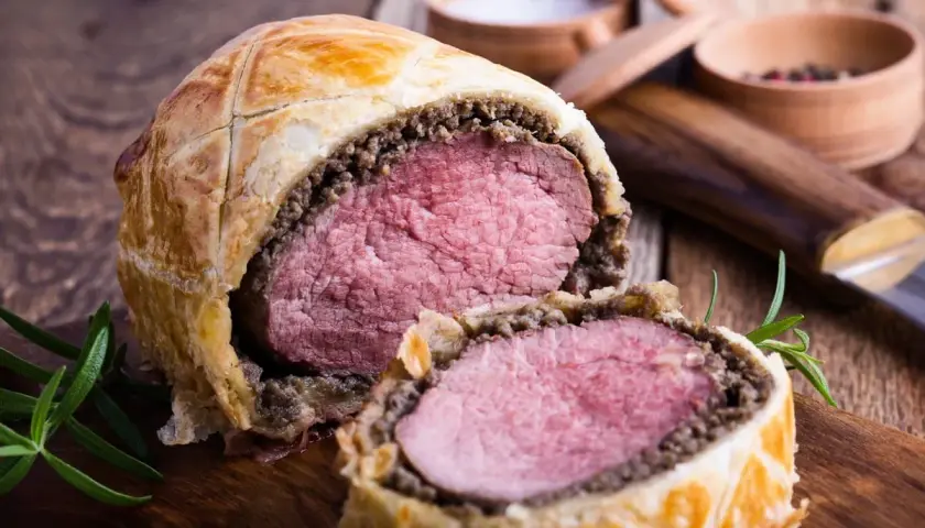 Un succulento filetto alla Wellington, tagliato a metà, rivela la sua carne rosa e tenera, avvolta in pasta sfoglia dorata e funghi.