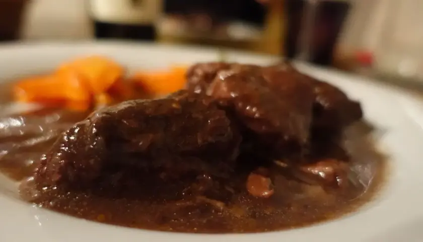 Un succulento brasato al barolo, tenero e profumato, accompagnato da carote arancioni su un piatto bianco.