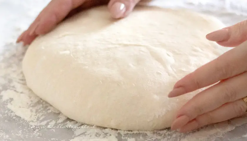 Mani che lavorano un impasto soffice, pronto per diventare una pizza giallo zafferano.