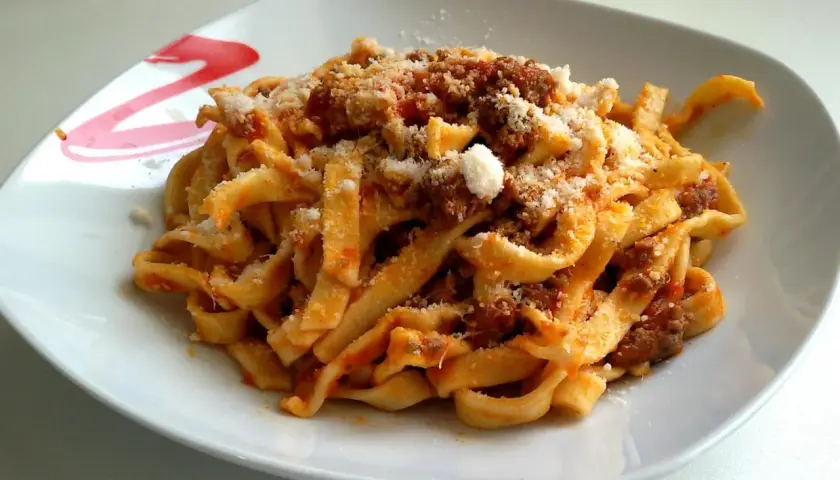 Un piatto di tagliatelle al ragù fumanti, condite con abbondante parmigiano grattugiato. Un classico della cucina italiana.