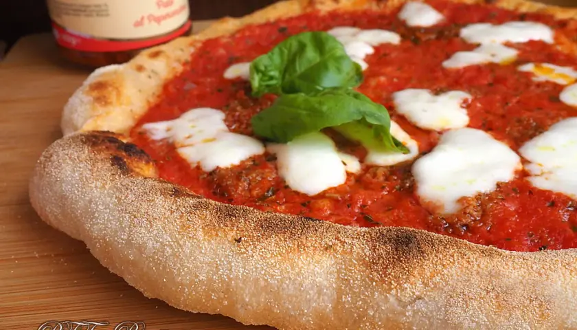 Pizza margherita con pomodoro, mozzarella filante e basilico fresco. La crosta dorata e alveolata è il risultato di una lunga lievitazione.