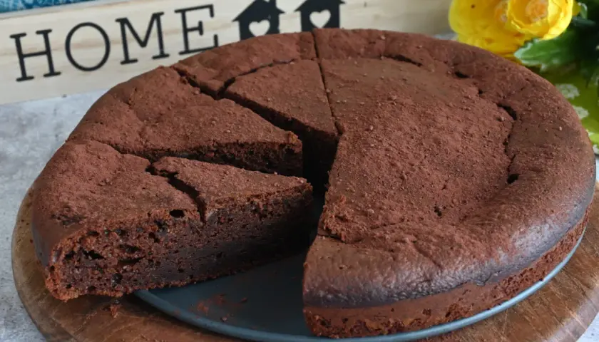 Un invitante dolce al cioccolato, cosparso di cacao, pronto per essere gustato. Sullo sfondo, una decorazione con la parola "HOME" e fiori gialli.