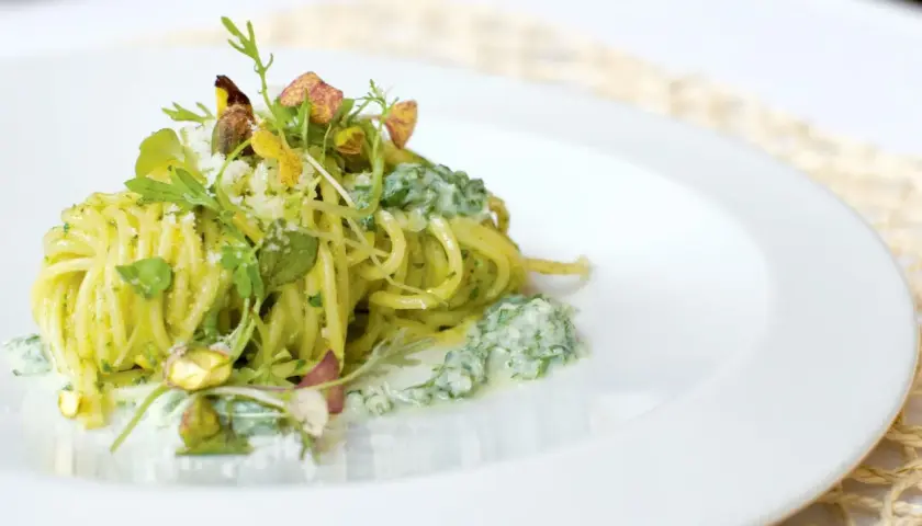 Spaghetti conditi con un cremoso pesto di pistacchi, guarniti con pistacchi interi e erbe fresche.