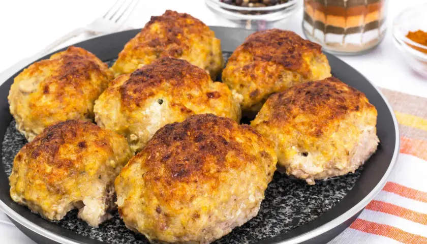 Golden brown zucchini and potato fritters on a black pan.