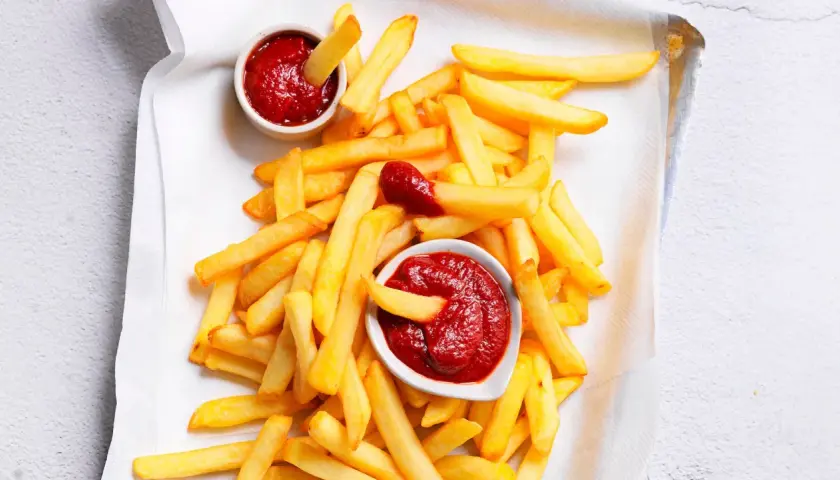 Patatine fritte dorate e croccanti con due ciotoline di ketchup fatto in casa, una con una patatina che si tuffa dentro.