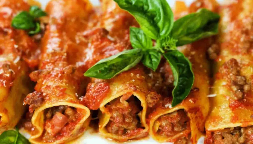 Cannelloni di carne ricetta della nonna, ripieni di ragù e conditi con sugo rosso e basilico fresco.