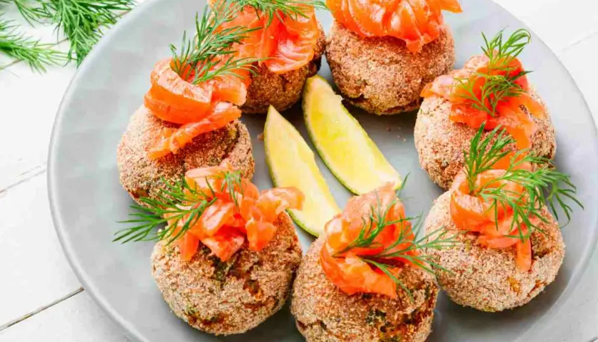 Polpette di pesce dorate, guarnite con salmone affumicato, aneto e spicchi di lime. Un antipasto raffinato e gustoso.