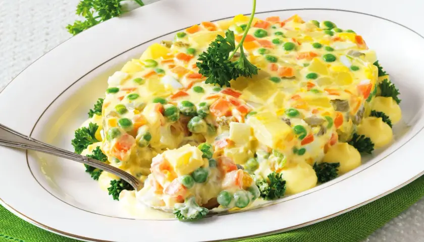 Insalata russa ricetta della nonna: un piatto cremoso con patate, carote, piselli e uova, guarnito con prezzemolo fresco.