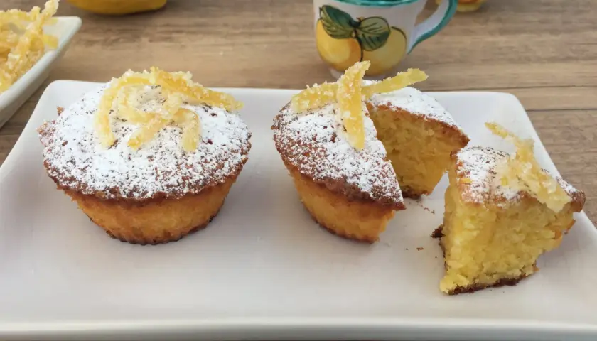 Deliziosi muffin caprese al limone, spolverati di zucchero a velo e decorati con scorzette candite.