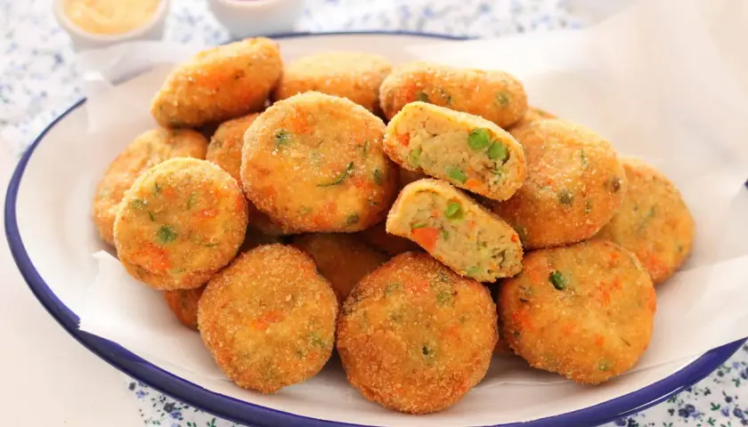 Un piatto pieno di polpette di verdure al forno, dorate e croccanti, con piselli e carote visibili all'interno.